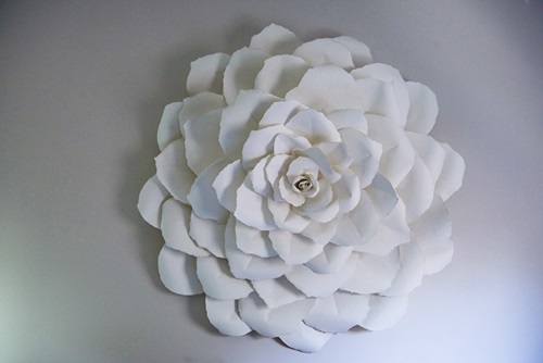 A round white flower made out of cut and assembled paper resembles a large dahlia.